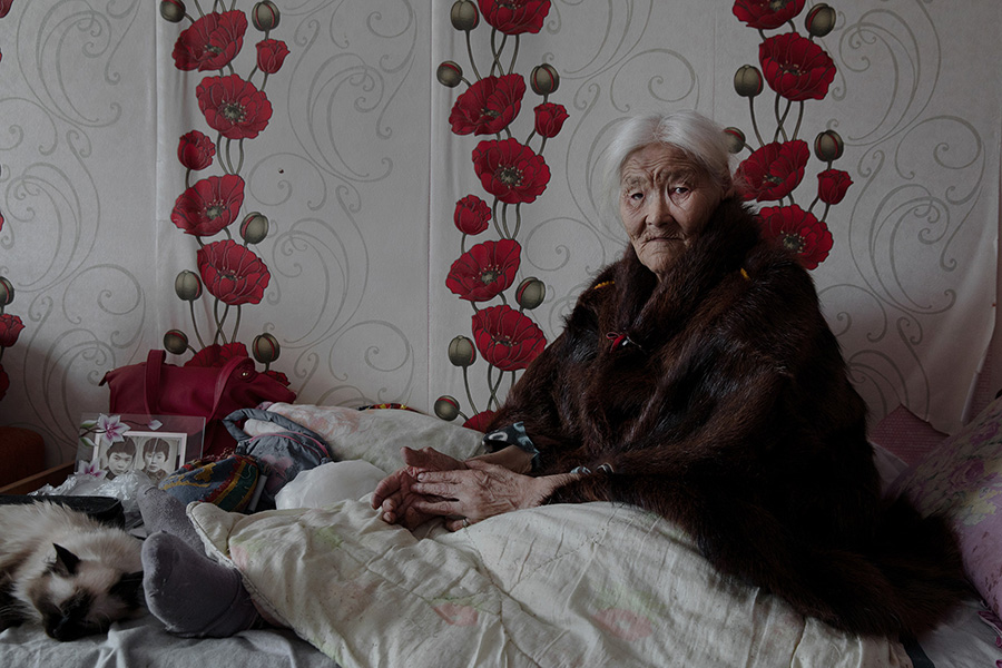 Necla Audi (Born. 1928). Yar-Sale village, Yamal Peninsula, Siberia, Russia. Although Necla was 89 when this portrait was taken, she declared that she insists on returning to live with the migrating community. At the far left of her bed, a picture of her two sons, taken when they were young. Now, both of them are herders in the tundra. 